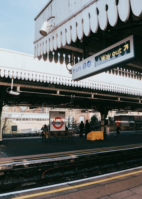 A view of multiple modern train carriages lined up at East Croydon station, with two yellow and grey passenger trains positioned on adjacent tracks, ready for departure or arrival. The scene is captured from an elevated perspective, showing several sets of railway lines extending into the distance, parallel to each other and separated by gravel beds. Overhead power lines are supported by tall metal poles that run alongside the tracks. In the background, there are urban buildings, including high-rise and mid-rise structures, with some trees and greenery visible further away. The sky is overcast, providing diffuse lighting across the scene. This railway environment, with its multiple tracks and urban surroundings, is relevant to the context of house removals and furniture transport, as transportation logistics often intersect with railway infrastructure for efficient moving services, such as those offered by Man With a Van Croydon.